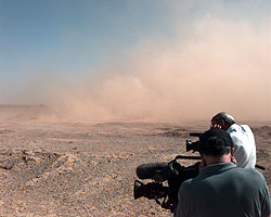 The media cover their ears as ThrustSSC kicks up the dust behind the test pan